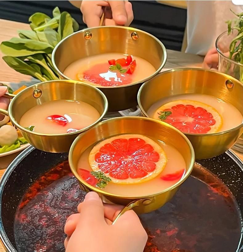 Gold kitchen bowl with handle for ramen filled with soup and garnished with grapefruit slices