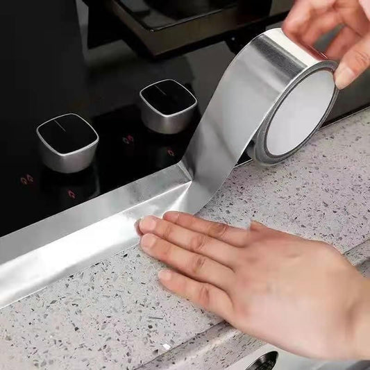 Applying silver fireproof adhesive tape for kitchen on countertop edge near stove knobs