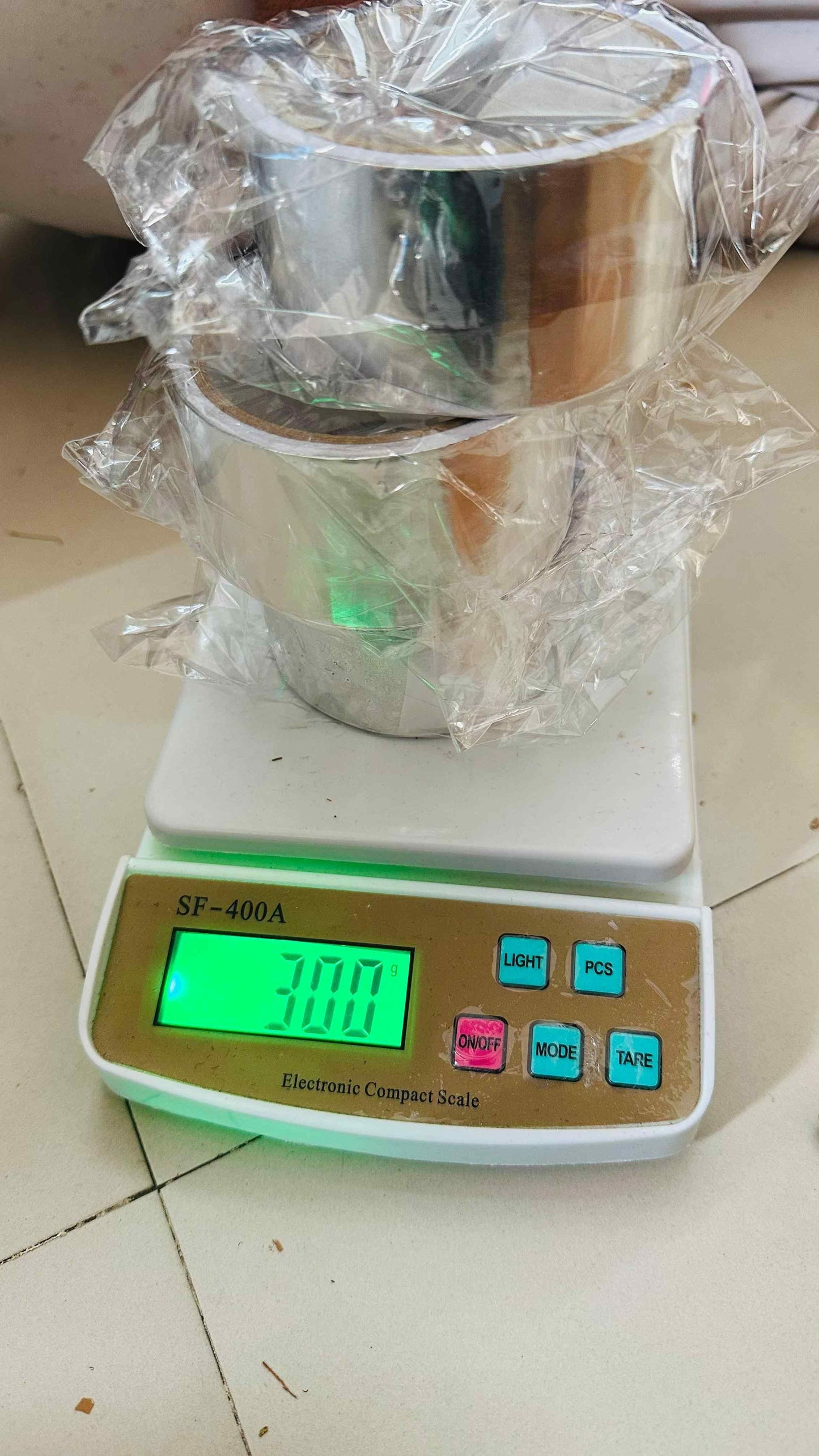 Three rolls of fireproof adhesive tape for kitchen stacked on an electronic compact scale showing weight 300 grams