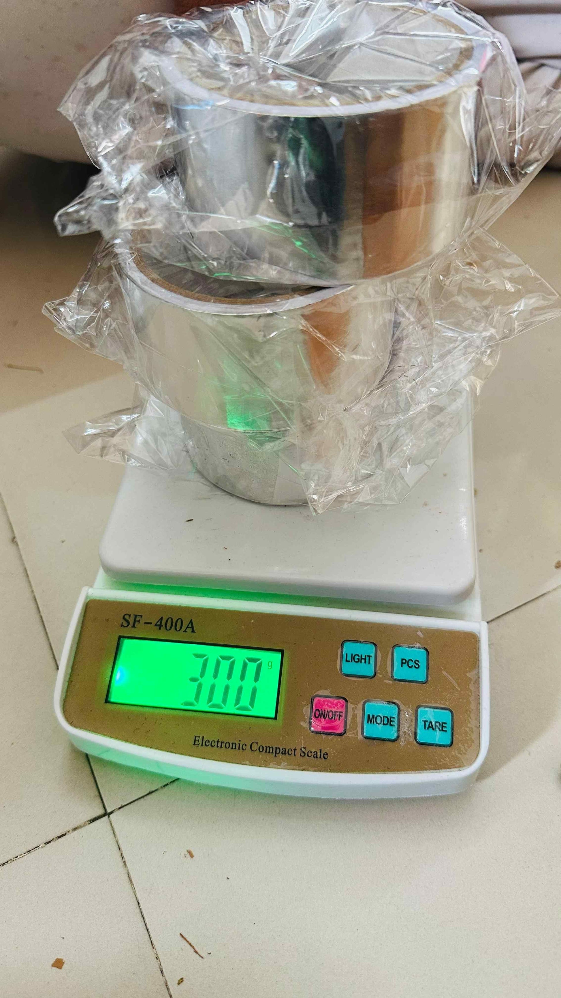 Three rolls of fireproof adhesive tape for kitchen stacked on an electronic compact scale showing weight 300 grams