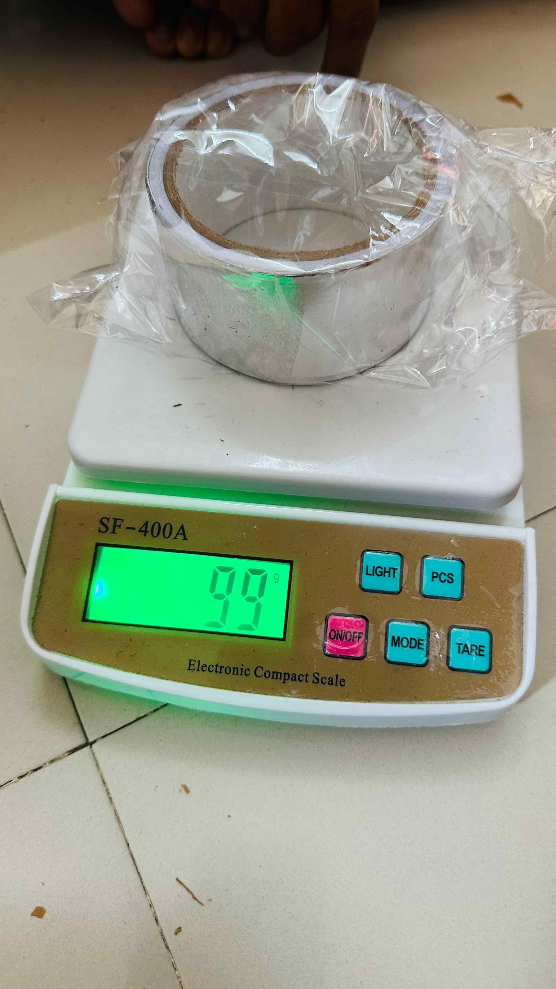 Roll of fireproof adhesive tape for kitchen placed on electronic compact scale showing 99 grams