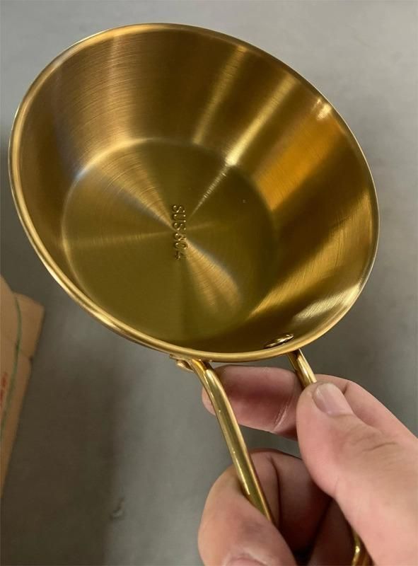 Hand holding a shiny gold kitchen bowl with handle for ramen with smooth brushed finish