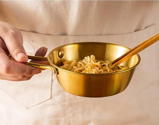 Gold kitchen bowl with handle for ramen held by hand with wooden chopsticks inside noodles